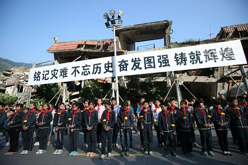 5月12日,在北川老县城地震遗址,小学生手拿菊花祭奠地震遇难者。新华社记者 王申 摄